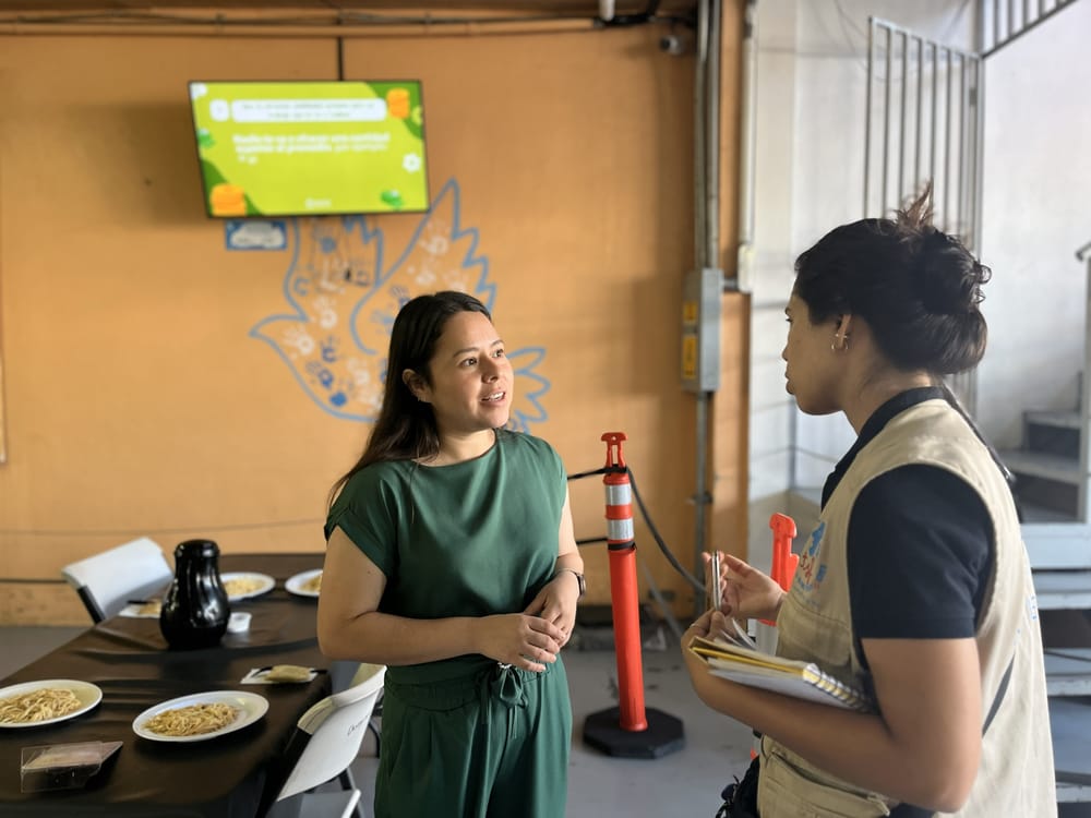 TSF et un responsable de refuge discutent, derrière eux, un écran affiche des informations essentielles pour les personnes en déplacement. Mexique, 2025.